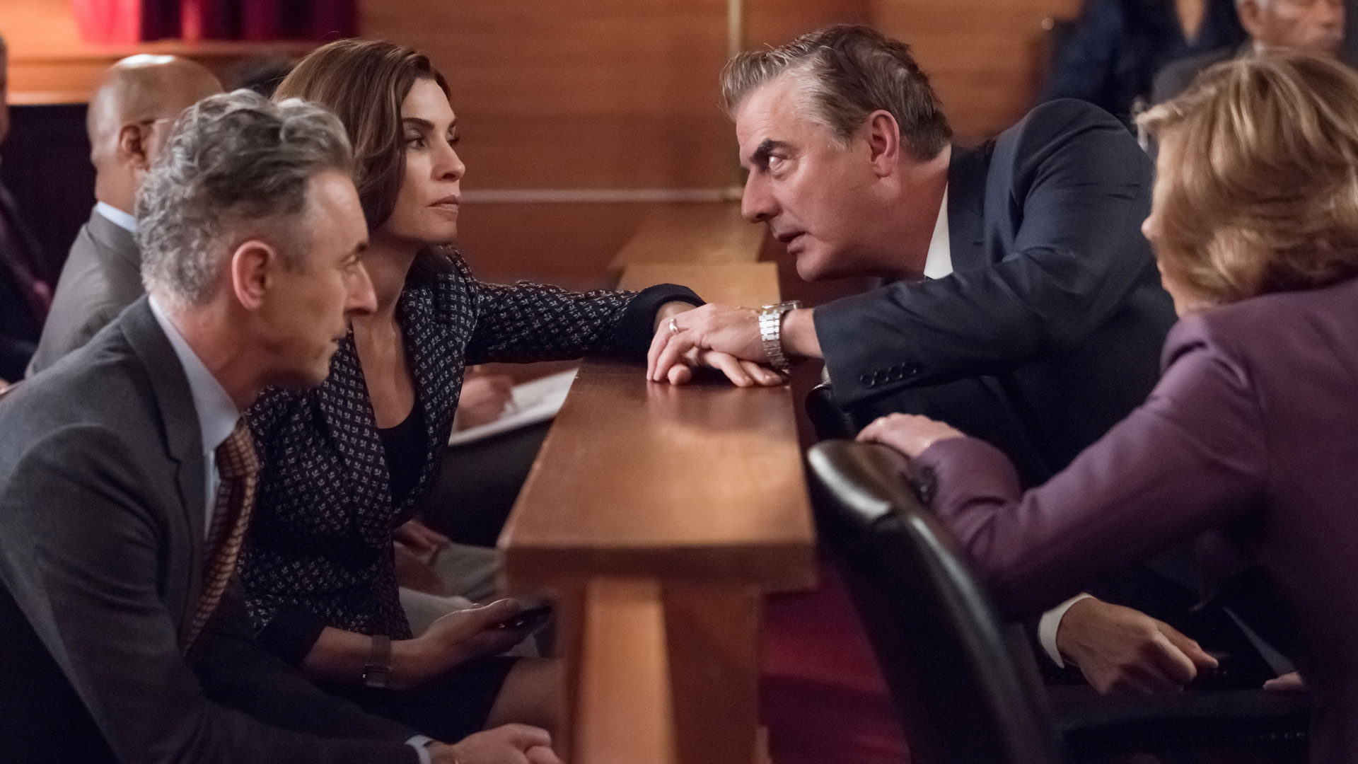 Peter grasps Alicia's hand in the courtroom.